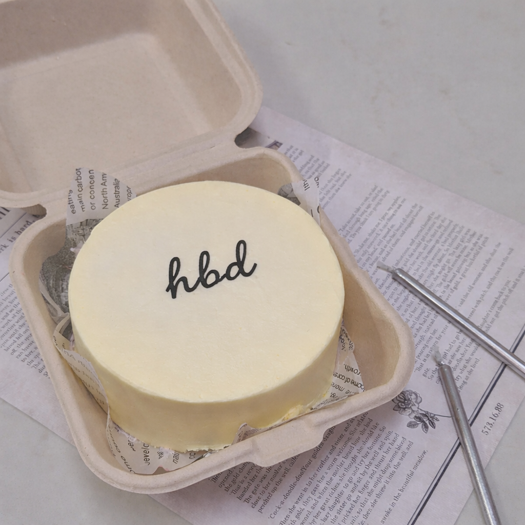 Cute pastel yellow cake with cursive lowercase 'hbd' black minimalistic text